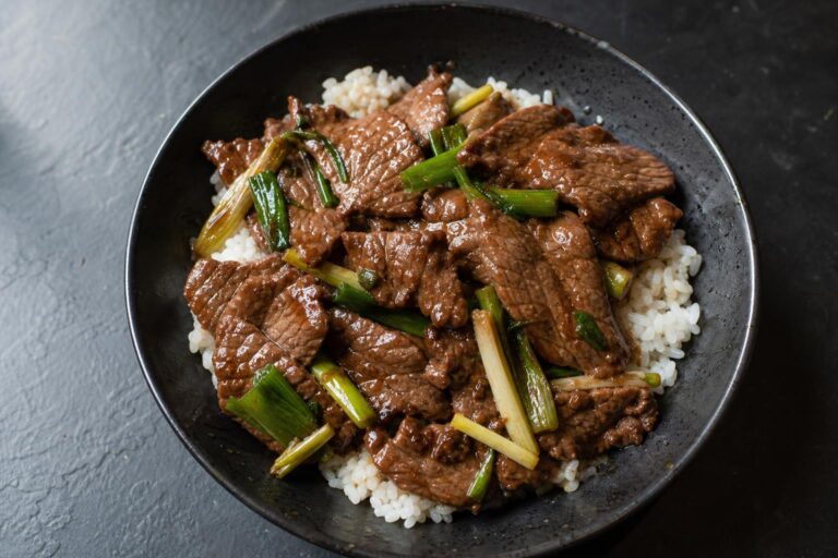 Mongolian beef with scallions over rice in a dark bowl