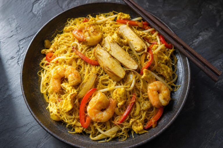 Singapore curry noodles with prawns, sliced chicken, egg and red pepper in a dark bowl