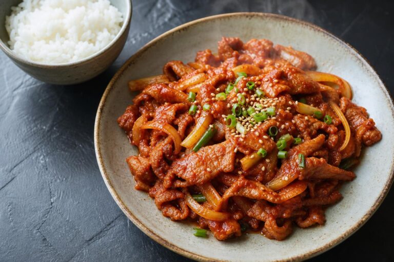 Korean spicy pork jeyuk bokkeum in a ceramic bowl with rice on a dark slate surface