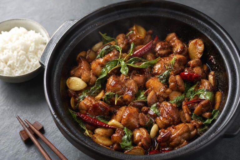 Taiwanese three cup chicken with basil and ginger in a clay pot with a bowl of rice