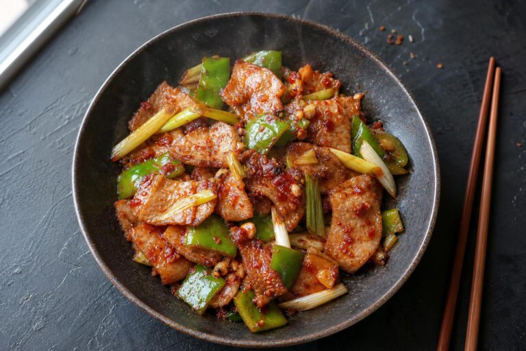 Overhead shot of lean twice cooked pork with leeks and green peppers in a glossy red sauce in a dark bowl