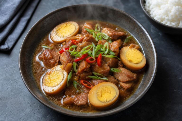 Vietnamese braised pork and eggs (thit kho) in caramel sauce with halved eggs, chili and scallions in a dark bowl