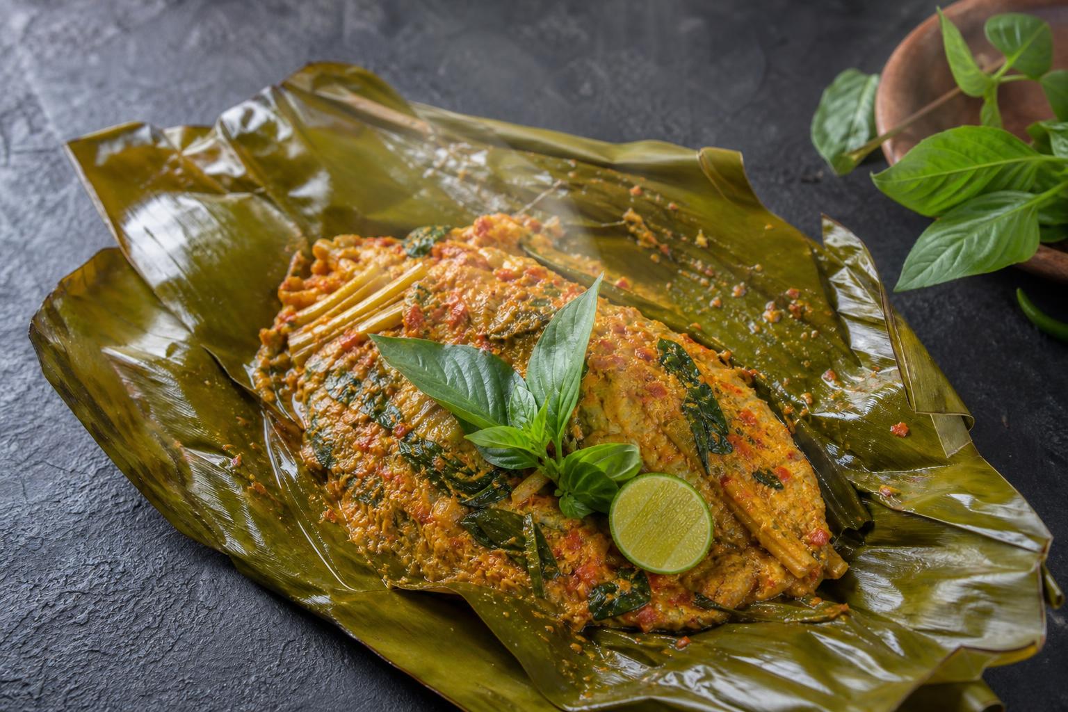 Indonesian pepes ikan, spiced steamed fish in banana leaf topped with lemon basil and a lime wedge