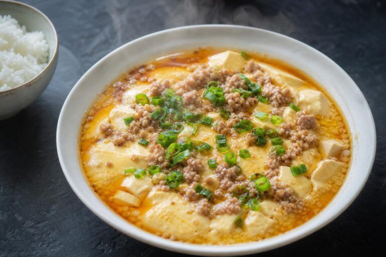 Chinese steamed egg custard topped with minced pork, silken tofu and scallions in a white bowl on dark slate